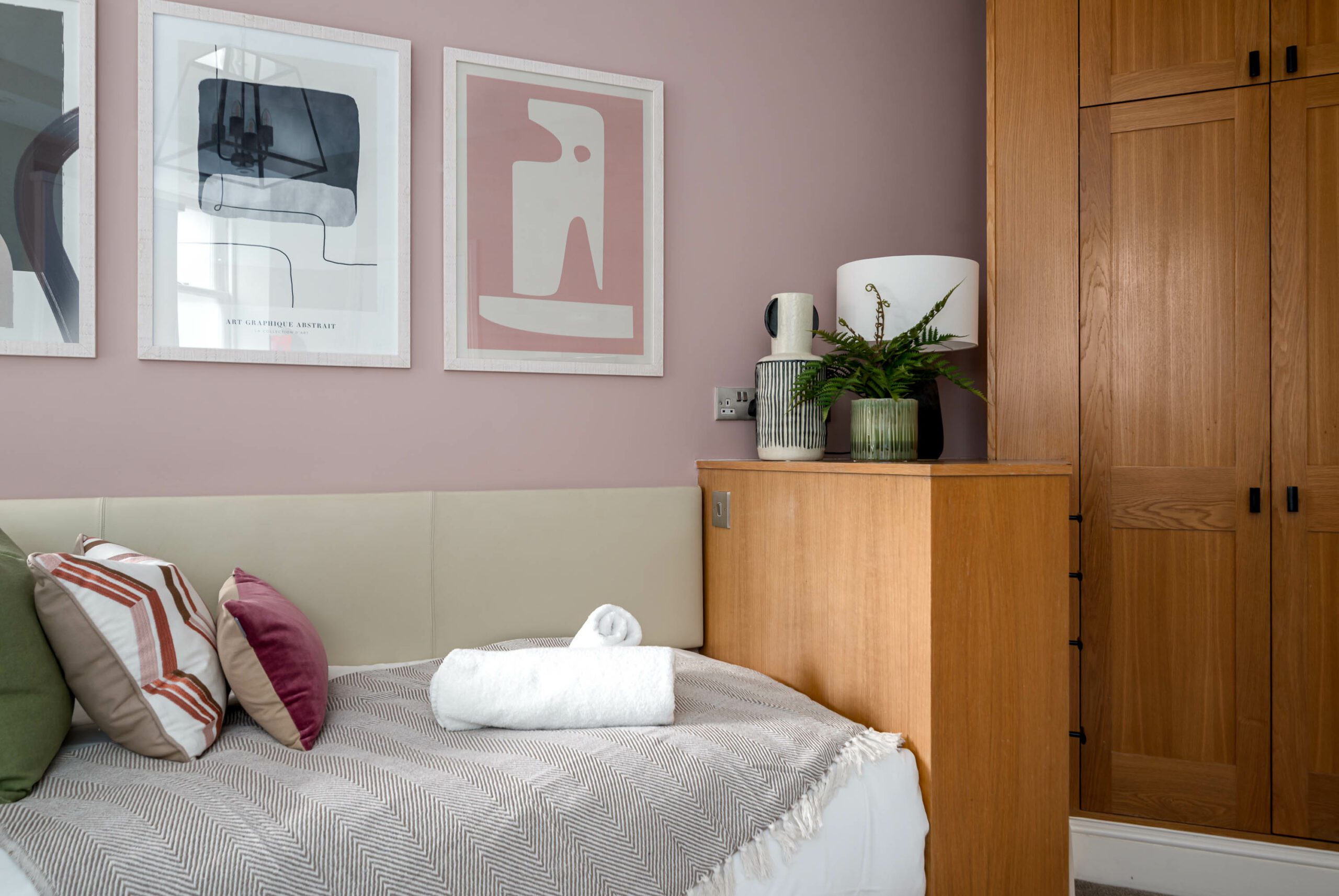 Close up of single bed against pale pink feature wall and abstract prints.