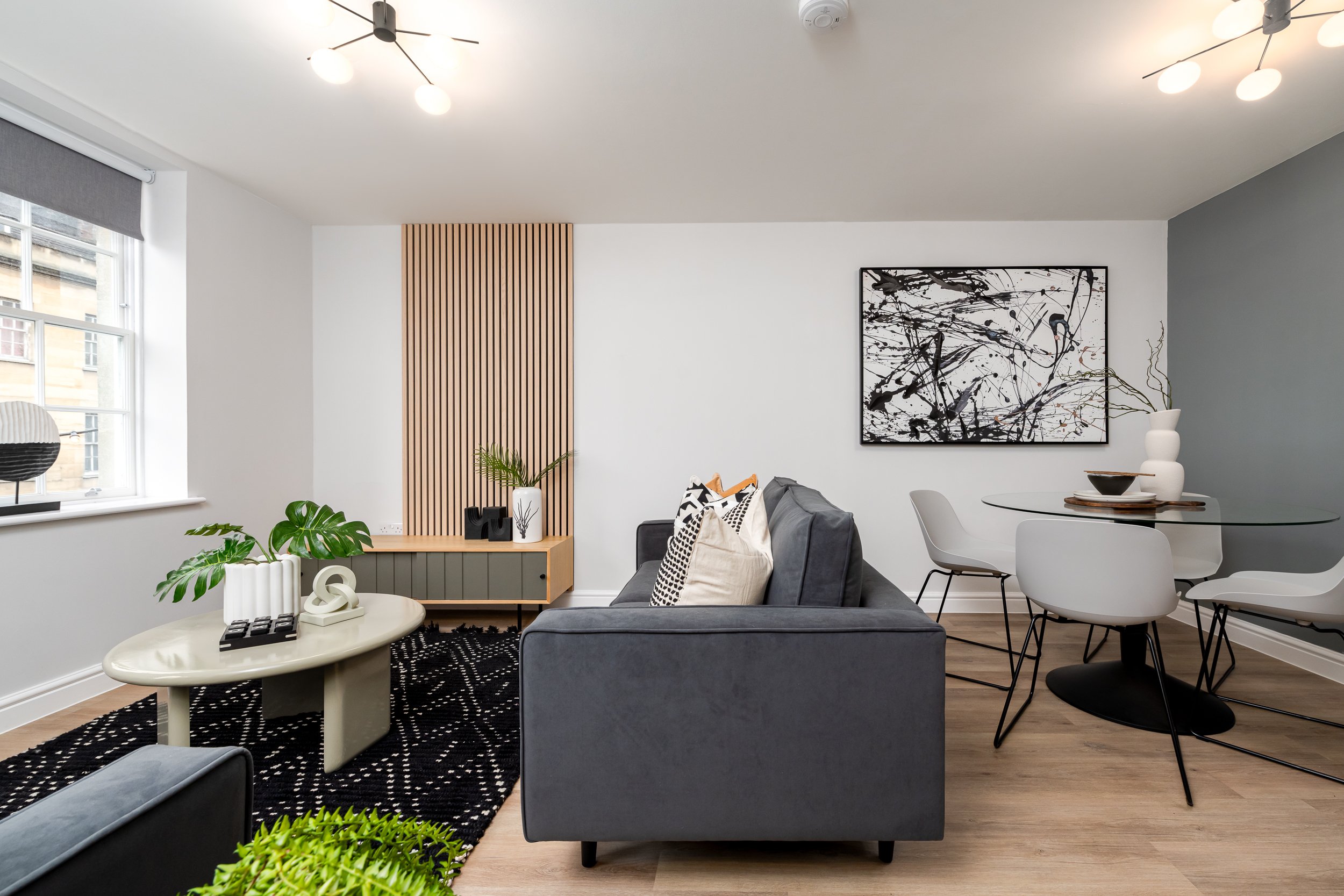 Side shot of living area with green sofa, grey artwork, feature wall and dining table.