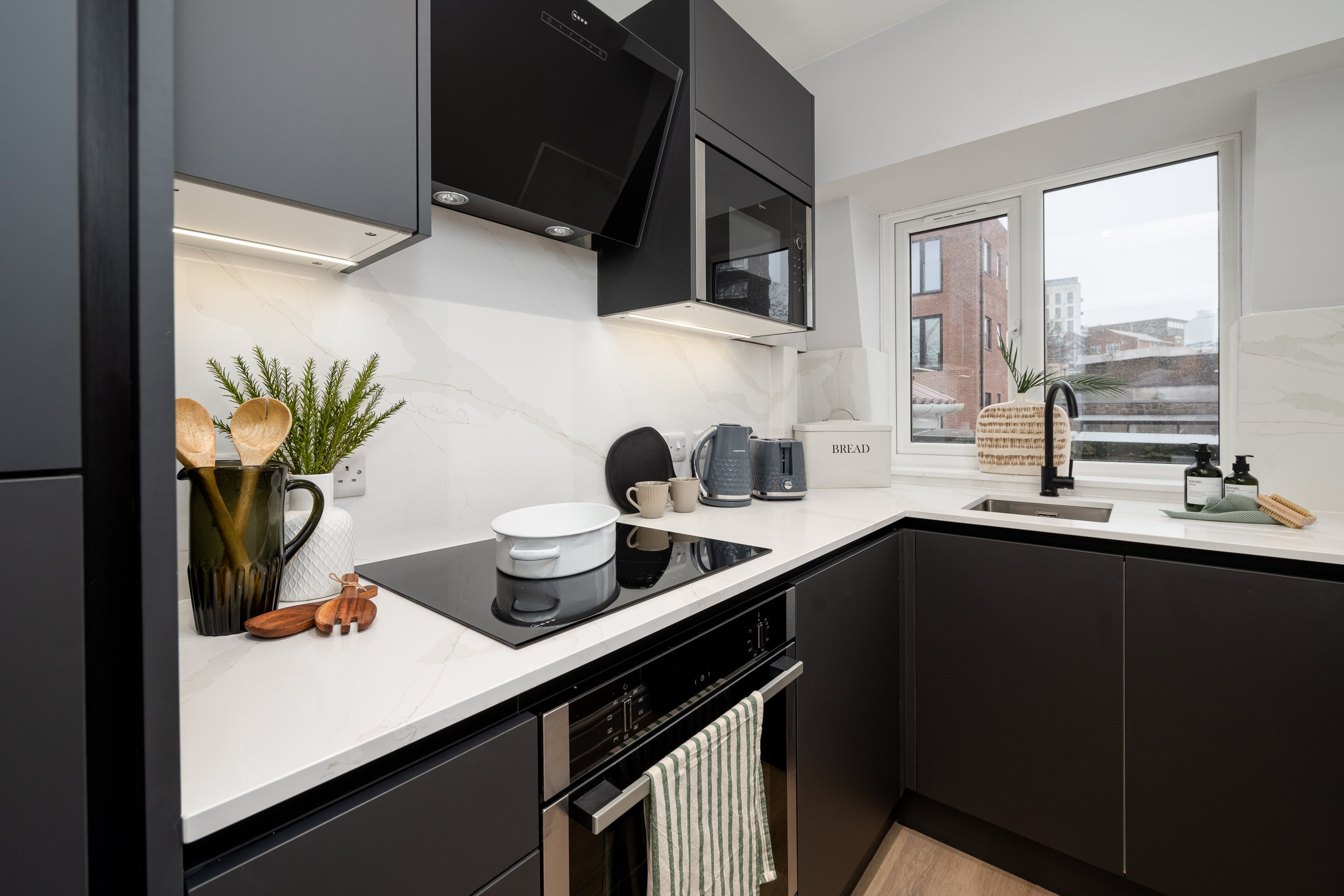 Dark grey modern kitchen with white marble worktops, oven, hob and extractor fan.