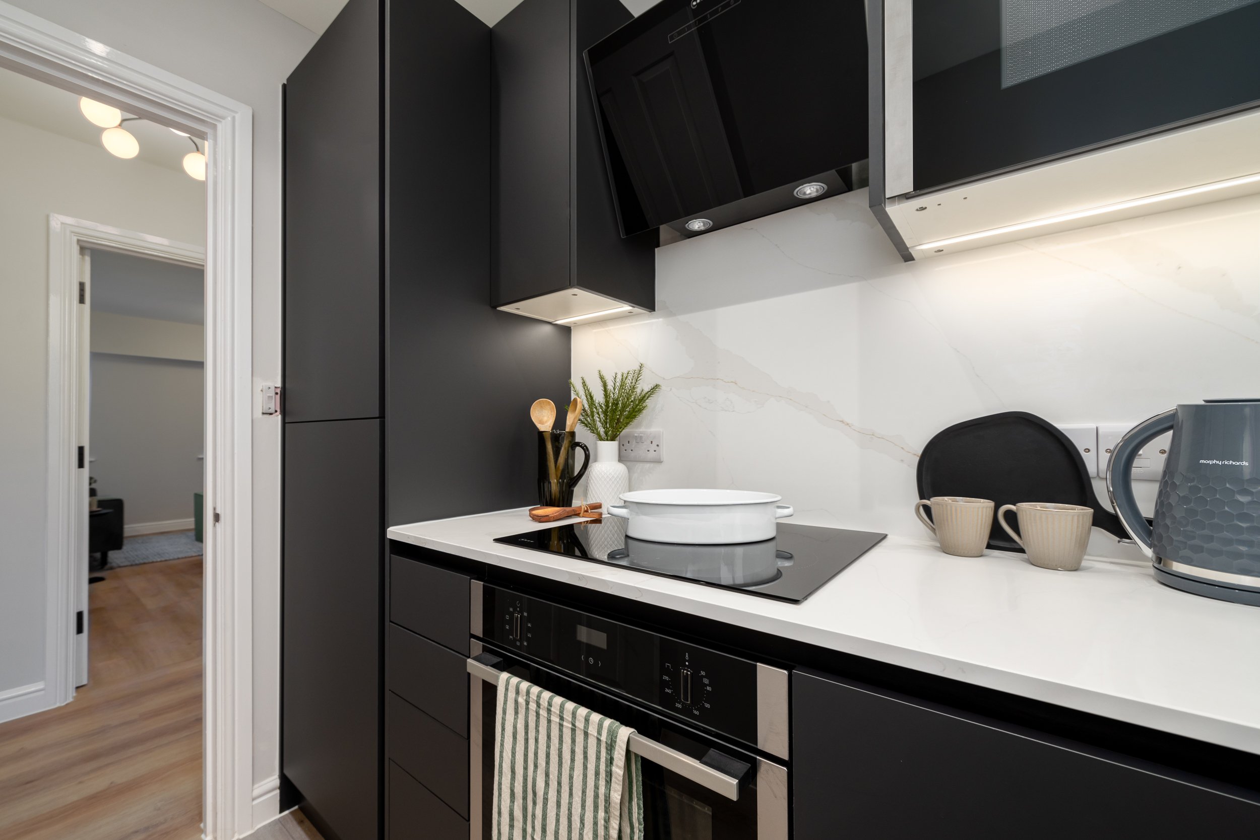 Dark grey modern kitchen with white marble worktops, oven, hob and extractor fan.