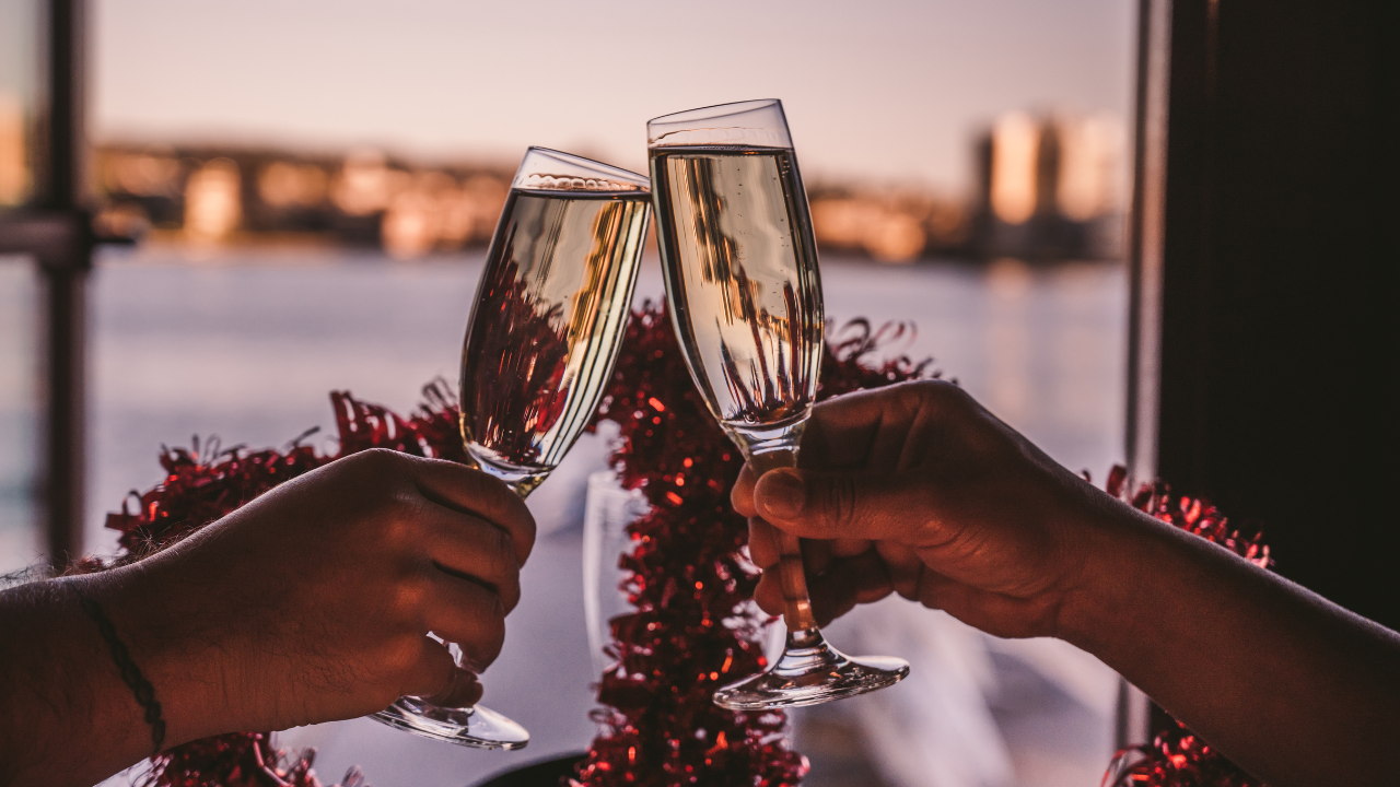 Two hands holding flute glasses of Prosecco, cheering one another against a sea view