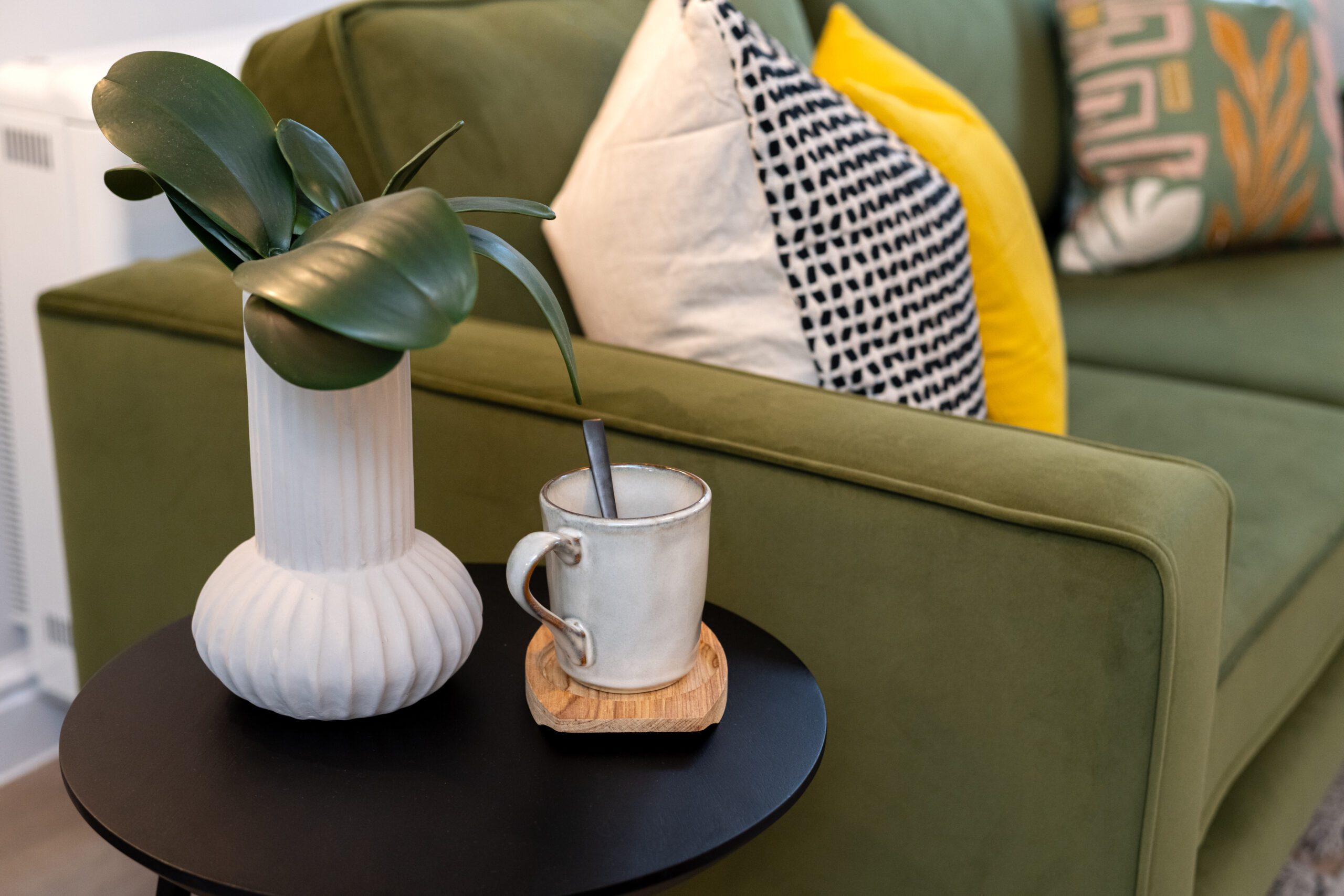 Close up of coffee table to the left of a green sofa with potted plant.