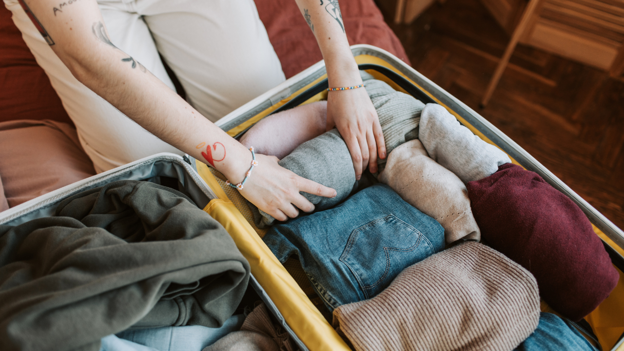 an open suitcase filled with clothes and two arms packing