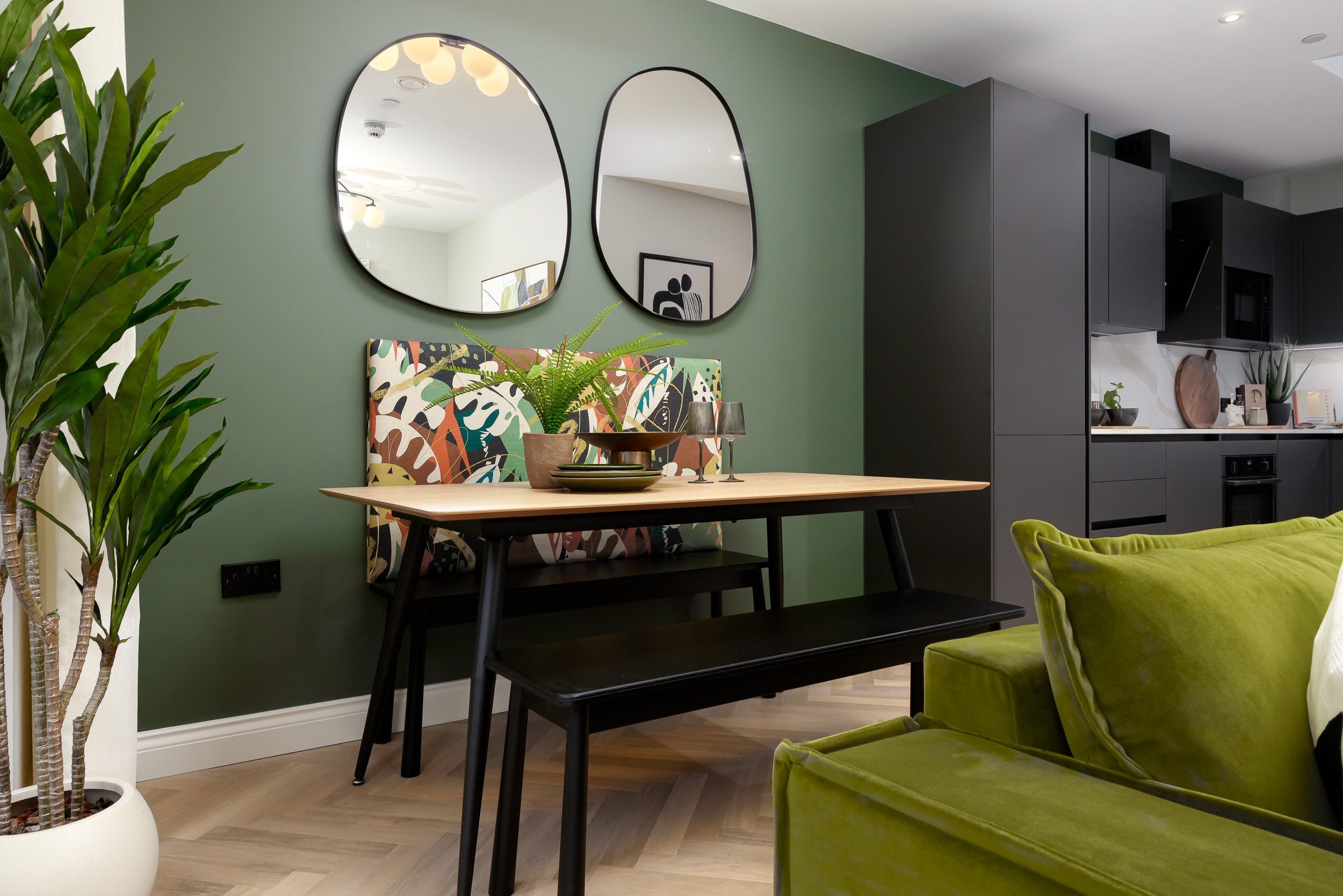 A green couch set in a living room, featuring a table and two mirrors reflecting the space.
